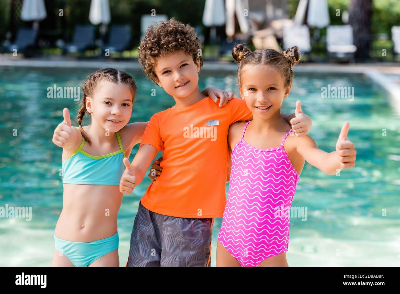 un petit garçon en t-shirt et des filles en maillot de bain montrant les  pouces près de la piscine Photo Stock - Alamy