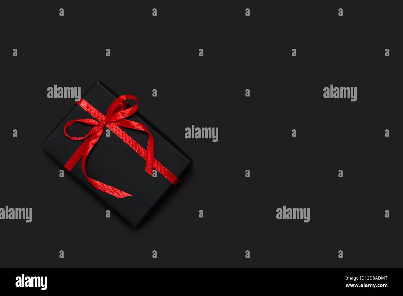 Concept de solde du Vendredi fou. Cadeau noir avec ruban rouge et noeud sur fond sombre. Modèle des fêtes avec cadeau de Noël, Saint-Valentin o Banque D'Images