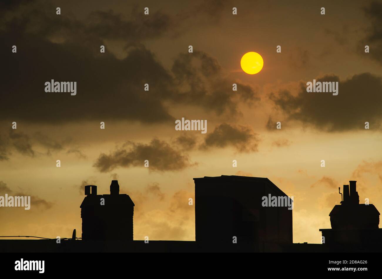Coucher de soleil avec un soleil jaune et des nuages sombres au-dessus des cheminées Banque D'Images
