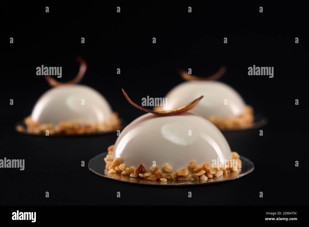 Foyer sélectif de gâteau blanc demi-sphère décoré de noix et de plumes de chocolat. Desserts aux surfaces lisses et glaçure miroir isolée sur fond noir. Délicieux plat sucré à la cafétéria. Banque D'Images