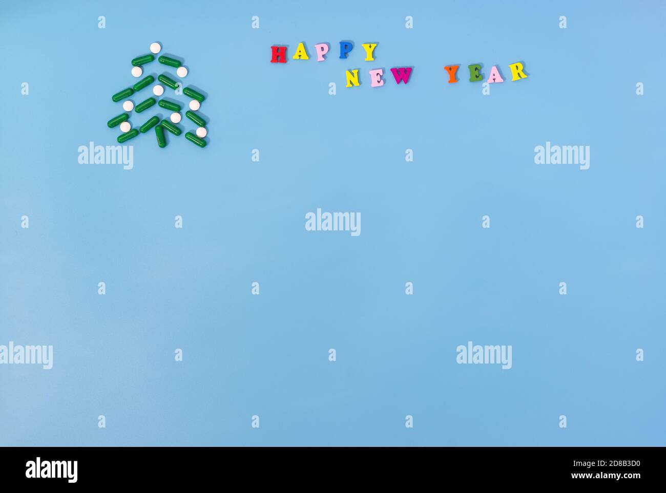 Un arbre de Noël fait de capsules vertes et de pilules blanches et l'inscription bonne année sur fond bleu. Le concept de vacances pendant le p Banque D'Images