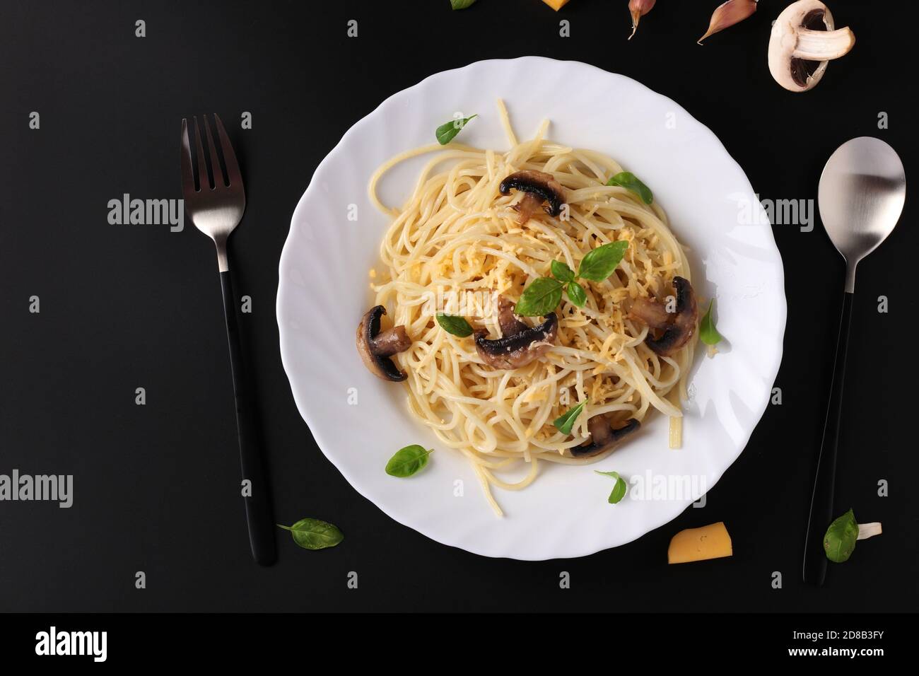 Spaghetti aux champignons et basilic sur plaque blanche sur fond noir, vue de dessus, espace pour le texte Banque D'Images