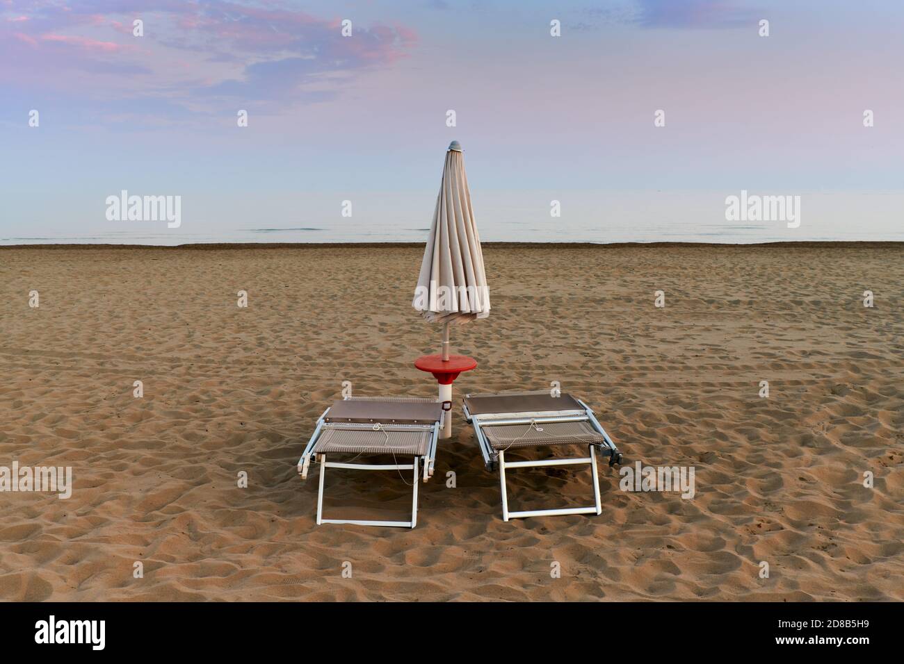 Deux chaises longues et un parasol fermés en face de la mer Adriatique à la fin de l'été dans une plage déserte. Banque D'Images