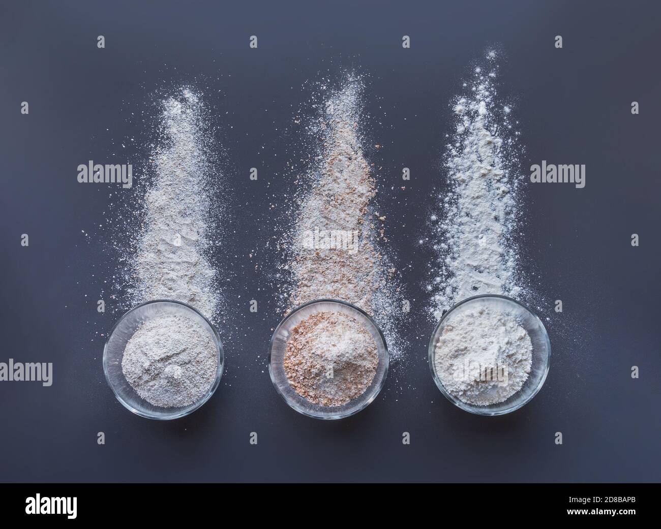 farines pour faire du pain dans des tasses en verre: seigle, blé complet, farine ordinaire ou polyvalente ou forte disposée sur fond gris Banque D'Images