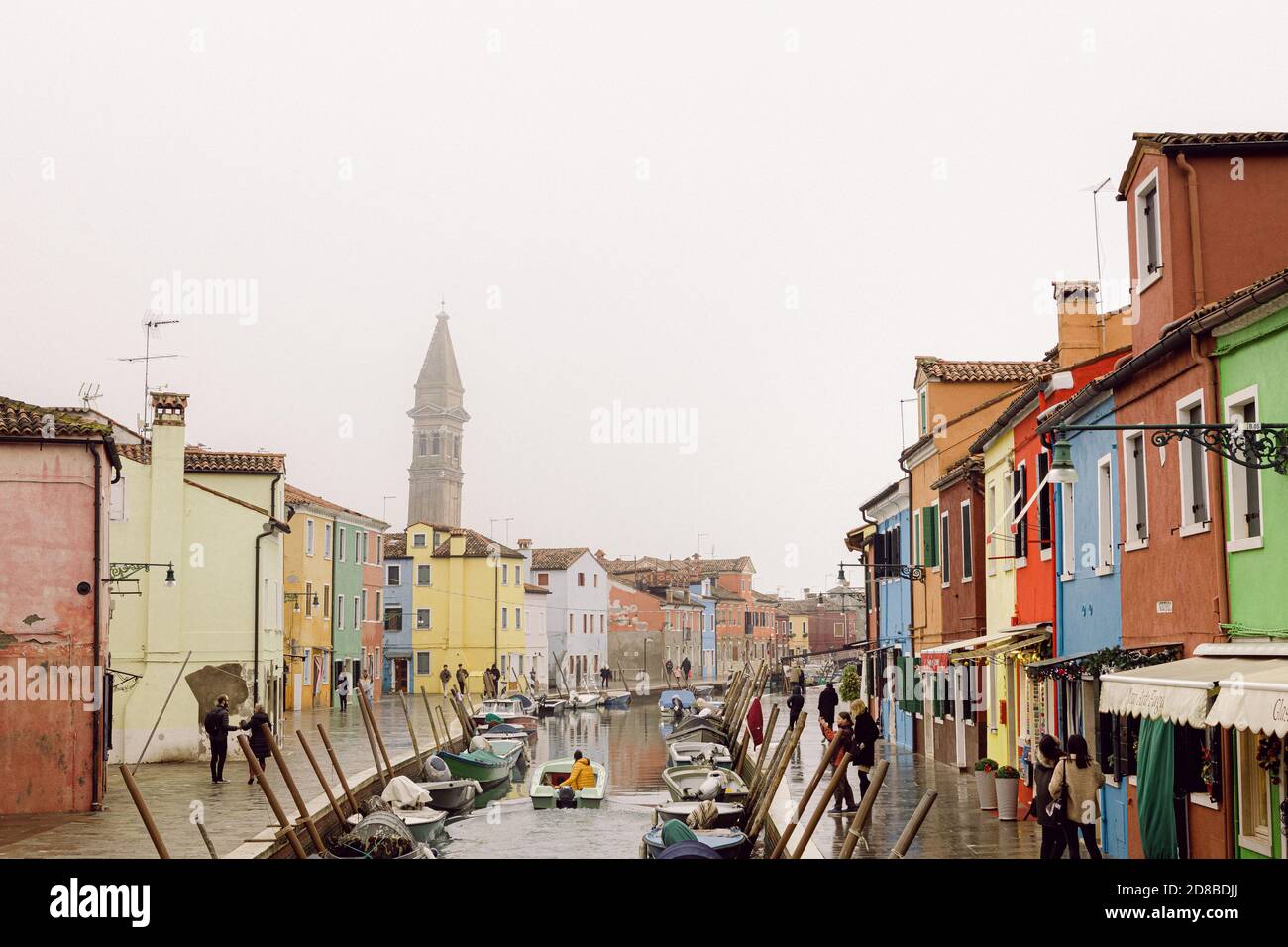 Maisons et canaux de Burano et Bell Tower de San Martino, Burano, avec des mouettes dans une journée d'hiver brumeux. Personne avec un imperméable jaune sur un petit bateau Banque D'Images
