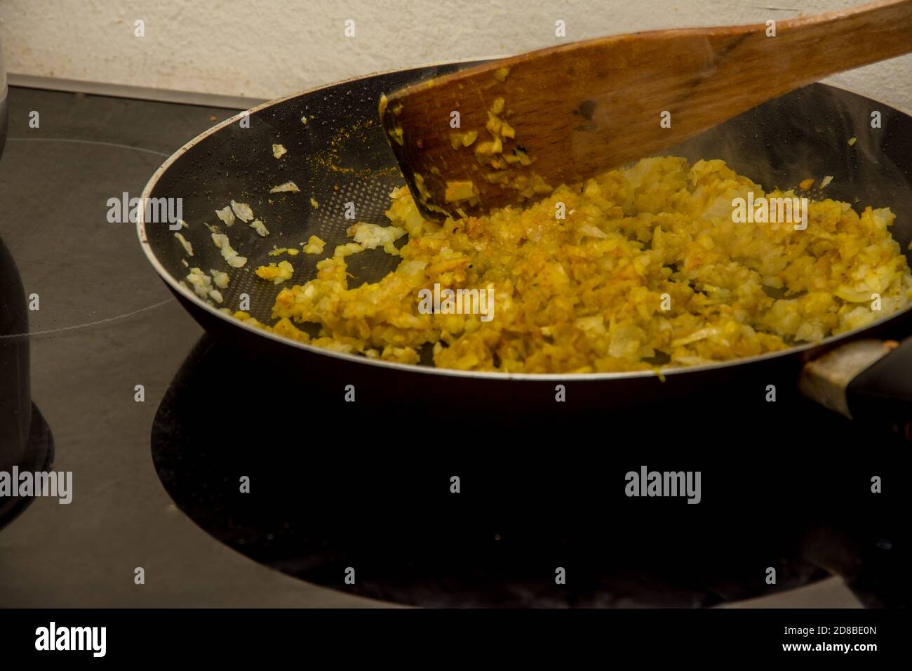 Mélanger et frire l'oignon avec des condiments orange et jaune indiens dans le récipient noir Banque D'Images