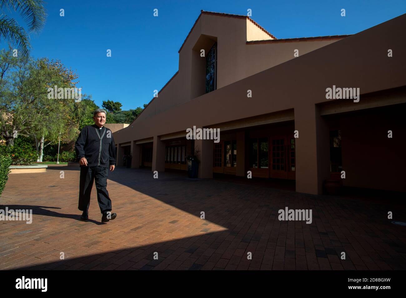 Le monseigneur d'une église catholique du sud de la Californie traverse la cour de l'église après le soleil et l'ombre. Banque D'Images