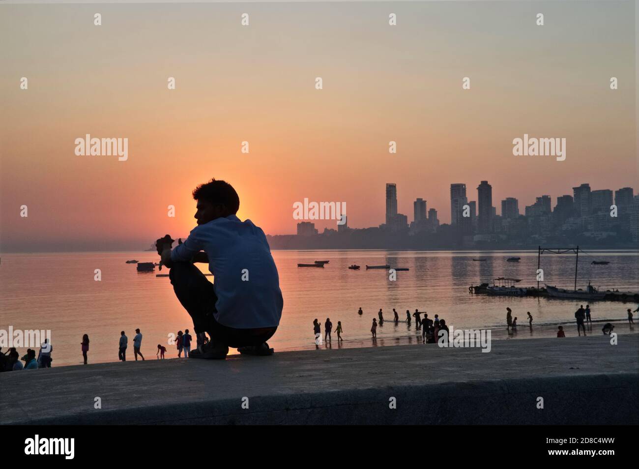 Un jeune Indien observe le coucher de soleil sur la mer d'Arabie tout en s'écrachant dans le style d'un village sur le remblai de Marine Drive, Mumbai, Inde Banque D'Images