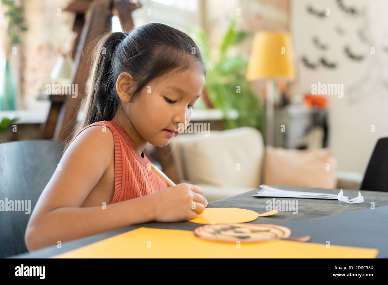 Une jeune fille asiatique créative concentrée assise à table et faisant du papier Artisanat de citrouille pour Halloween en studio d'art Banque D'Images