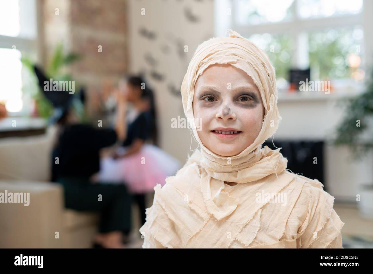 Portrait d'un garçon souriant avec un visage blanc enveloppé Les bandages comme une momie debout dans la chambre décorée pour Halloween partie Banque D'Images