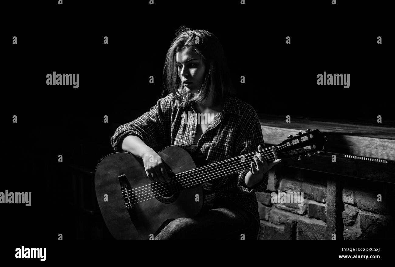 Femme jouant de la guitare, tenant une guitare acoustique dans ses mains. Jeu de guitariste fille. Fille joue de la guitare. Femme hipster homme assis dans un pub. Noir Banque D'Images