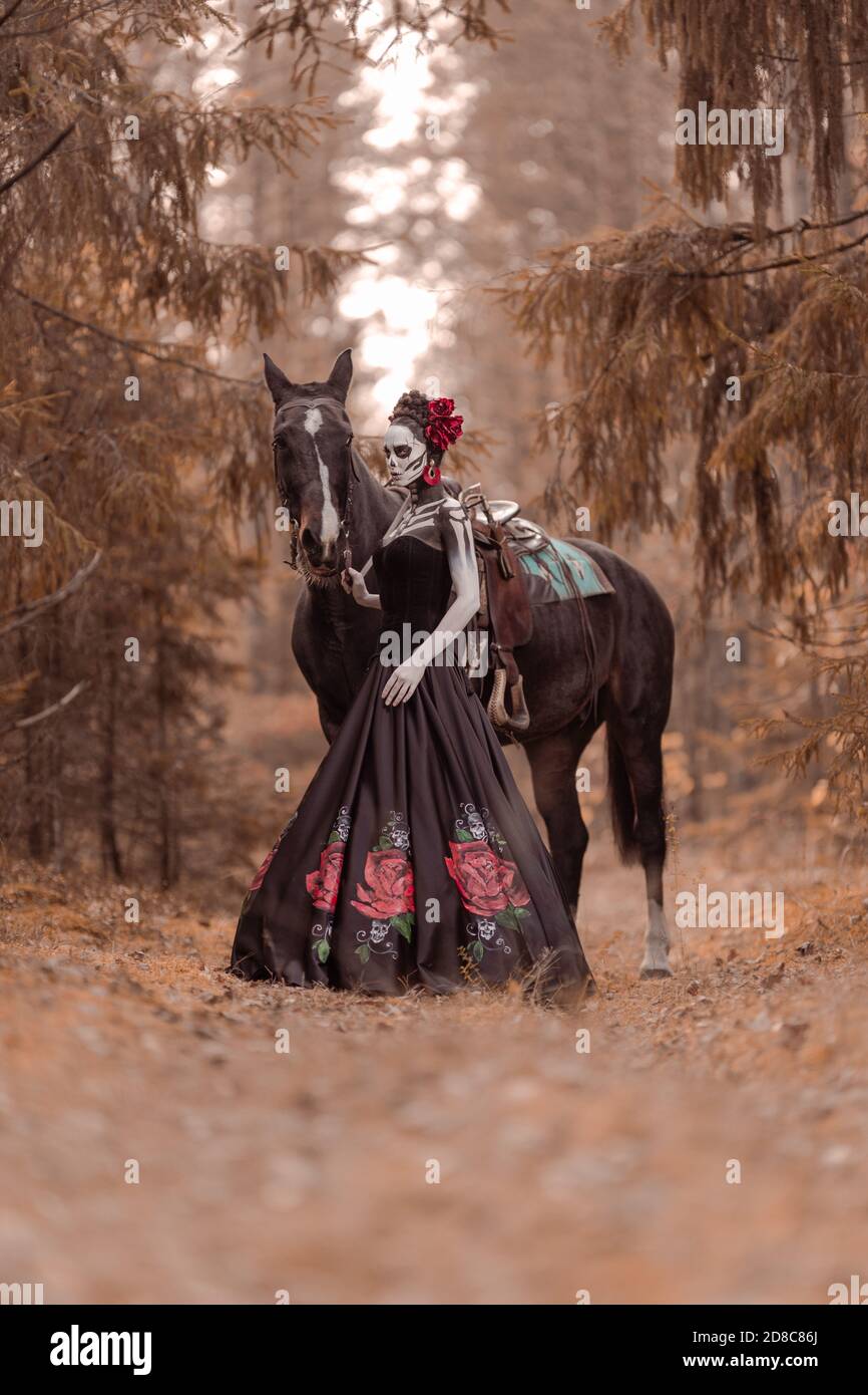 Jeune femme habillée comme le symbole mexicain de l'époque du calavera mort dans une robe noire et un homme avec des armes dans ses mains posant dans la forêt wi Banque D'Images