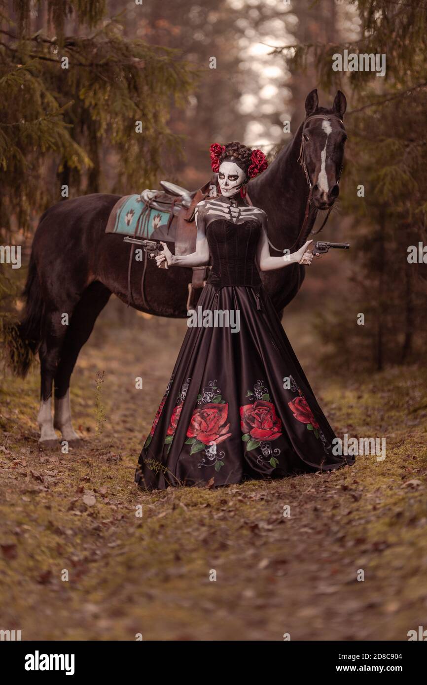 Jeune femme habillée comme le symbole mexicain de l'époque de la calavera morte dans une robe noire posant dans la forêt avec un cheval Banque D'Images