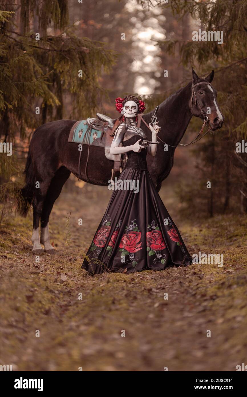 Jeune femme habillée comme le symbole mexicain de l'époque de la calavera morte dans une robe noire posant dans la forêt avec un cheval Banque D'Images