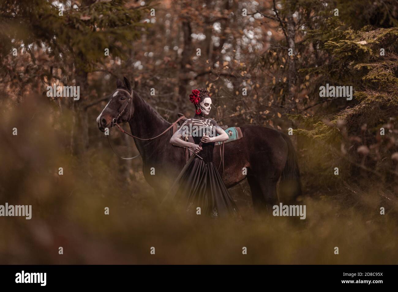 Jeune femme habillée comme le symbole mexicain de l'époque de la calavera morte dans une robe noire posant dans la forêt avec un cheval Banque D'Images