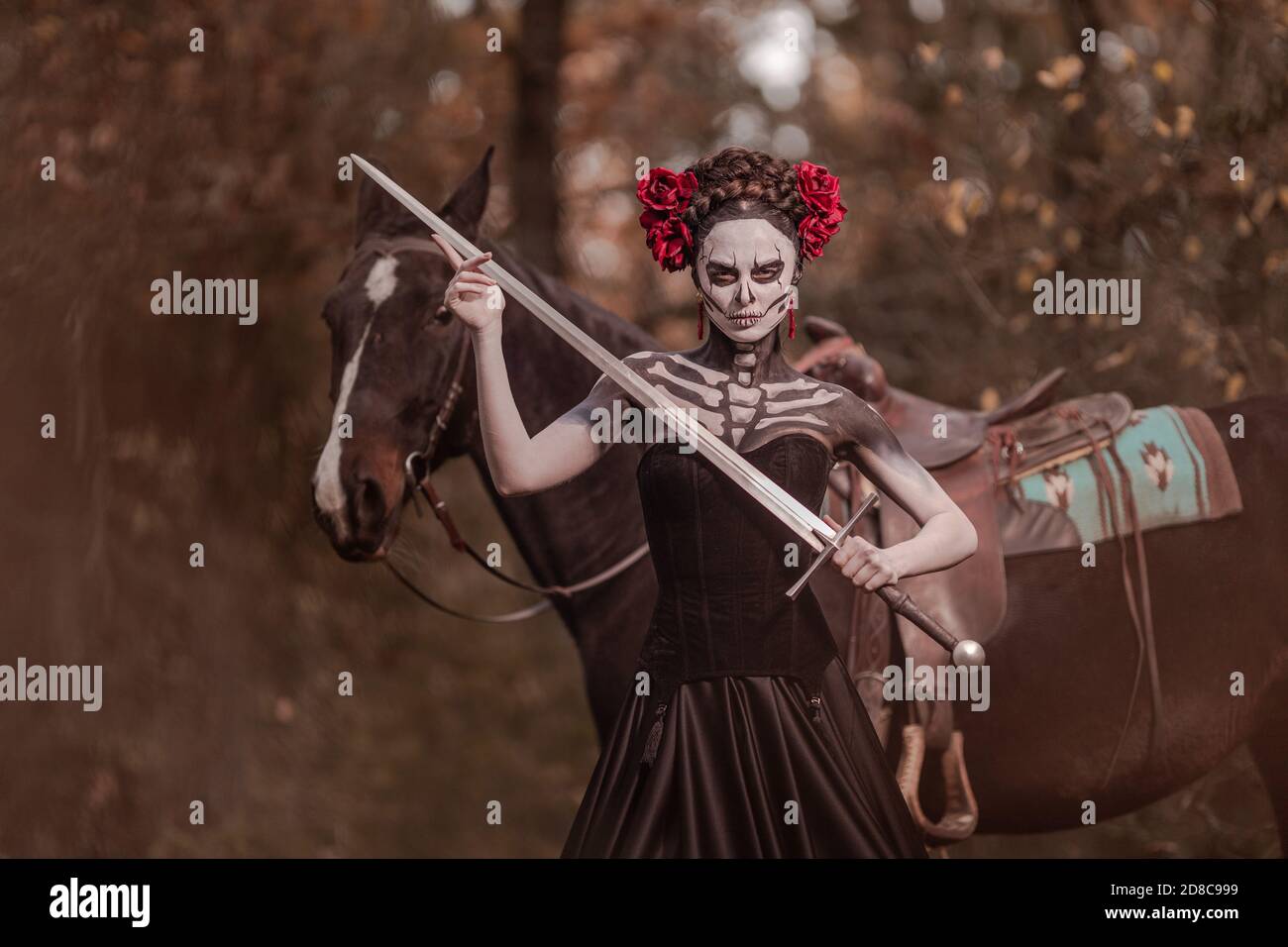 Jeune femme habillée comme le symbole mexicain de l'époque de la calavera morte dans une robe noire posant dans la forêt avec un cheval Banque D'Images