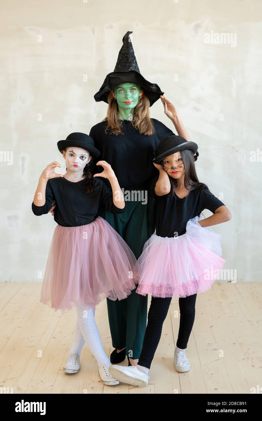 Portrait d'une femme sérieuse à face verte en sorcières chapeau posant avec mime mime mime mignon grimacing contre le mur gris Banque D'Images