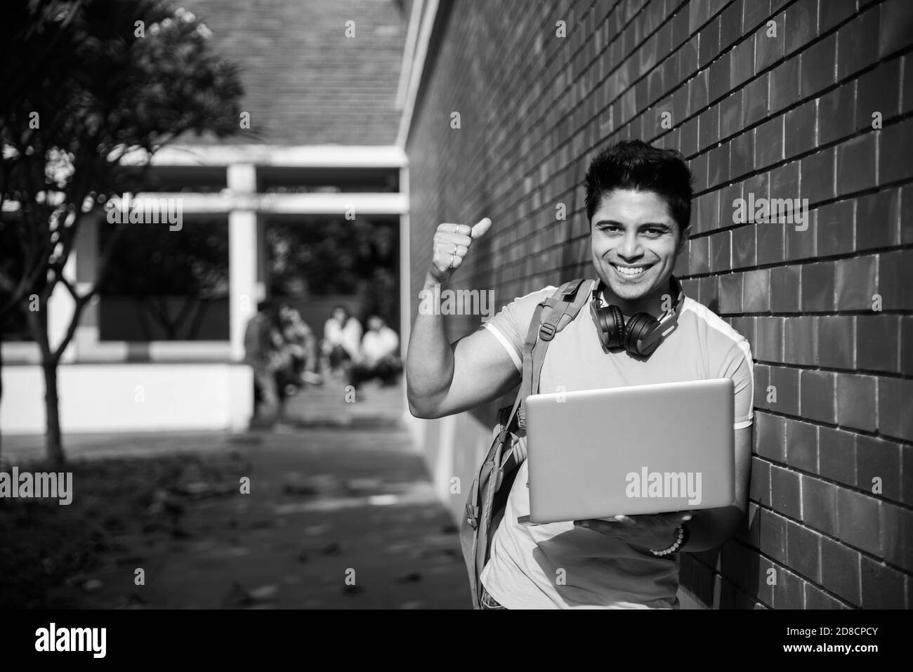 Un étudiant indien d'Asie se concentre sur un ordinateur portable ou un livre de lecture tandis que d'autres camarades de classe en arrière-plan, une image en plein air sur le campus universitaire Banque D'Images