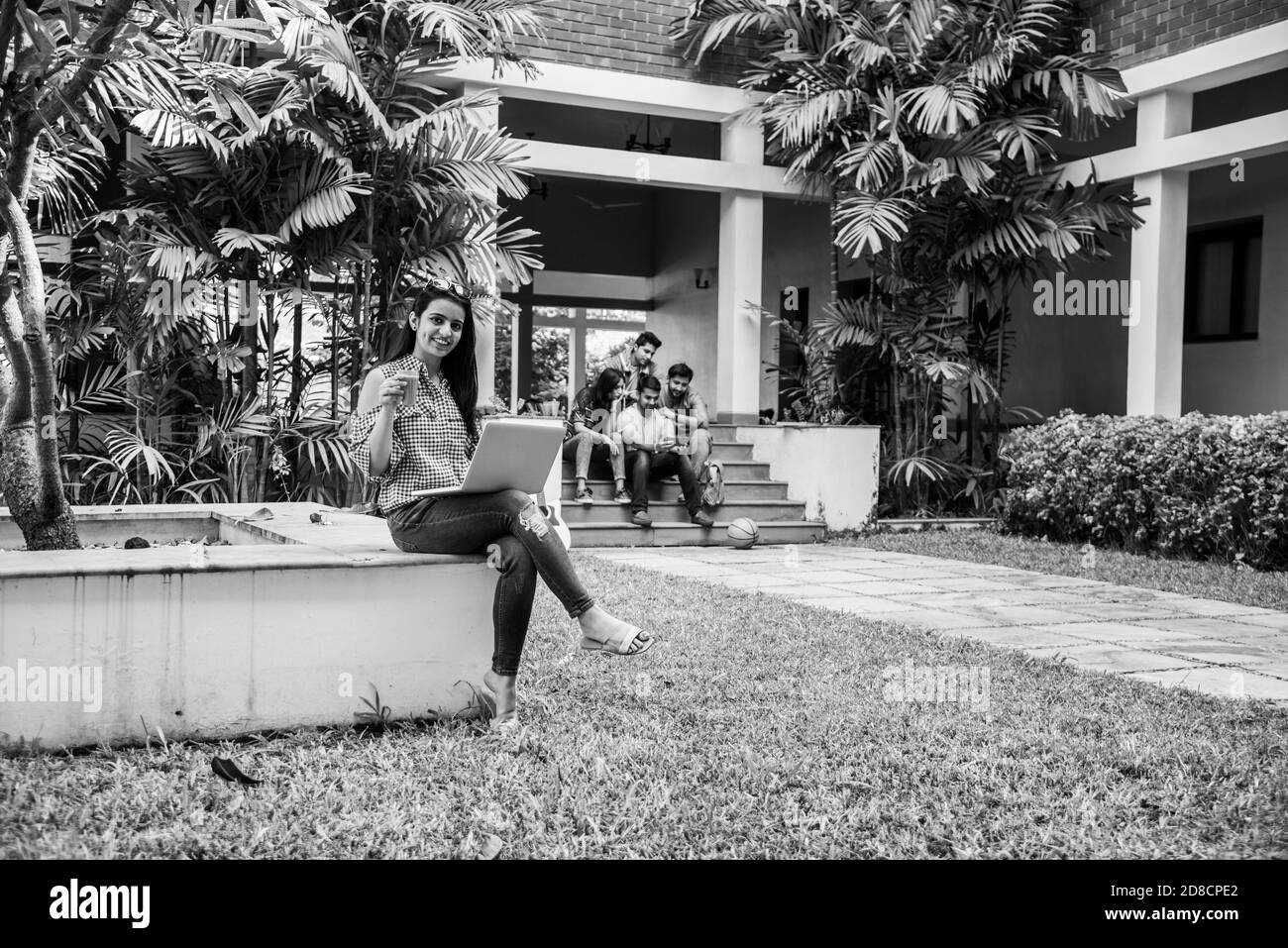 Un étudiant indien d'Asie se concentre sur un ordinateur portable ou un livre de lecture tandis que d'autres camarades de classe en arrière-plan, une image en plein air sur le campus universitaire Banque D'Images