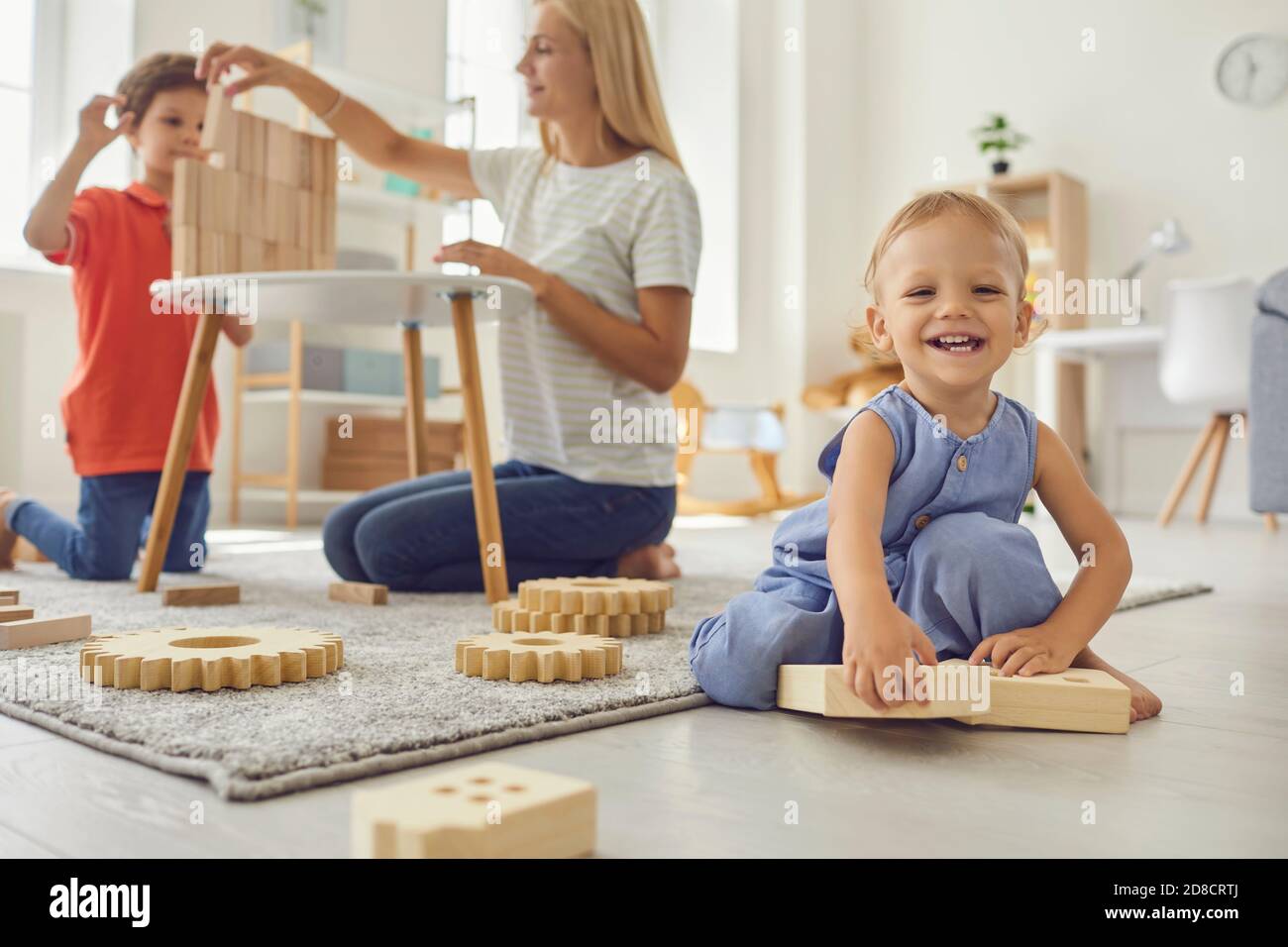 Mignon petit enfant regardant l'appareil photo et souriant pendant l'aîné frère et maman jouent en arrière-plan Banque D'Images