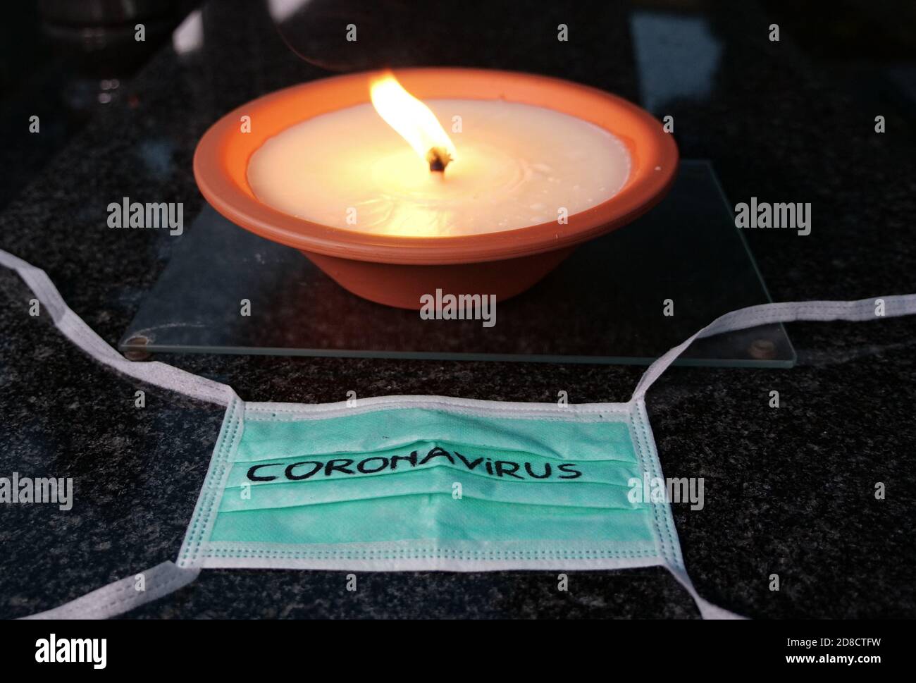 Concept d'éclosion de coronavirus. Décès causé par le coronavirus, victime du virus Covid-19. Lumière de bougie et masque médical à la tombe dans le cimetière. Banque D'Images
