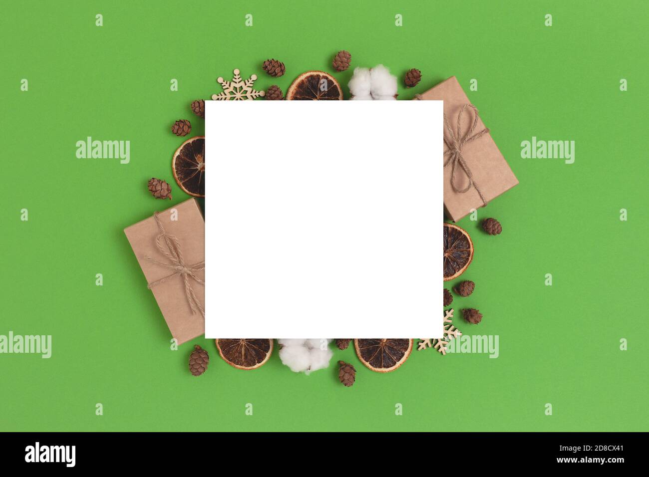 Carte en papier vide avec cadre en cadeaux et décorations de Noël naturels. Maquette carrée sur fond vert. Banque D'Images