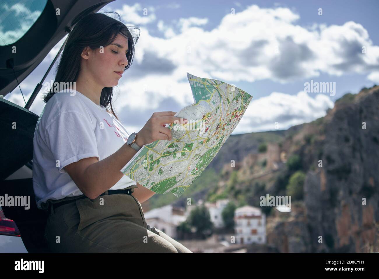 Une jeune fille assise sur le coffre de sa voiture regarde sur la carte pour de nouvelles destinations à explorer. Concept de photographie de voyage. Prise de vue panoramique. Banque D'Images