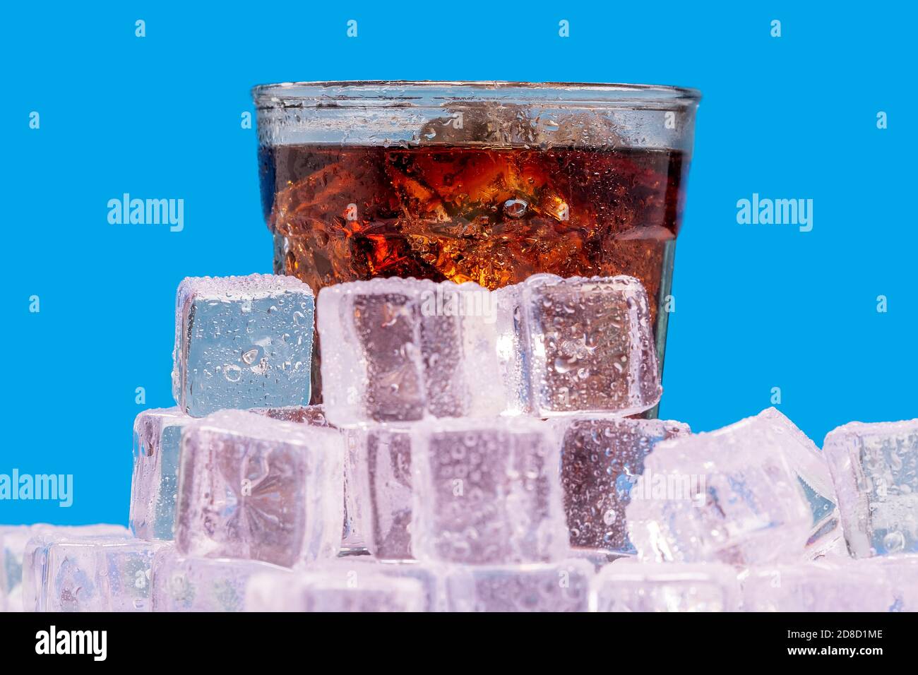 Verre froid glacé de cola, soda, boisson gazeuse pop entouré de glaçons avec condensation sur un fond bleu. Banque D'Images