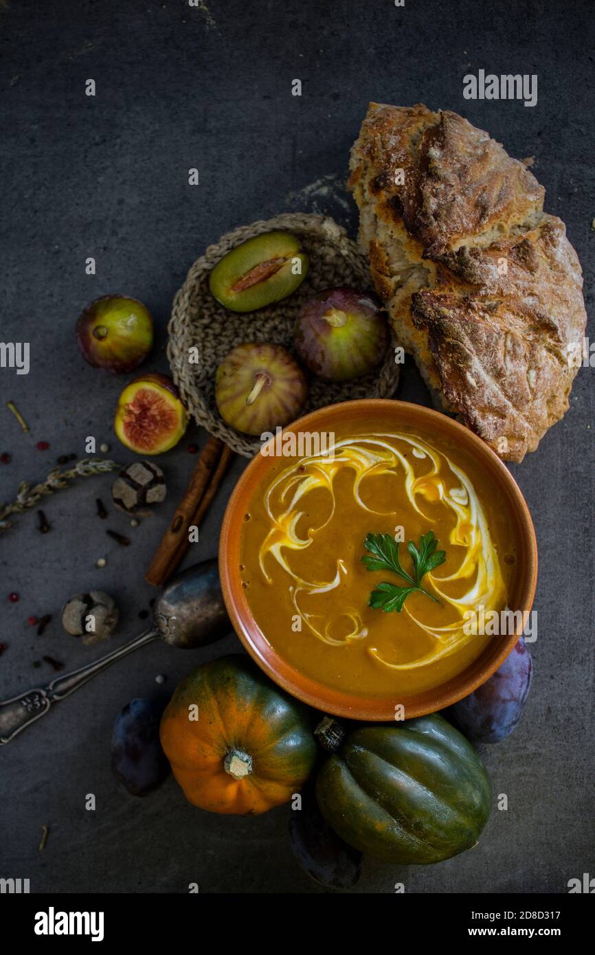 Menu d'automne. Vue de dessus photo d'un bol avec soupe de potiron, cendre de pierres précieuses, romarin, poivre, pain frais et cuillère d'argent. Arrière-plan gris foncé. Banque D'Images