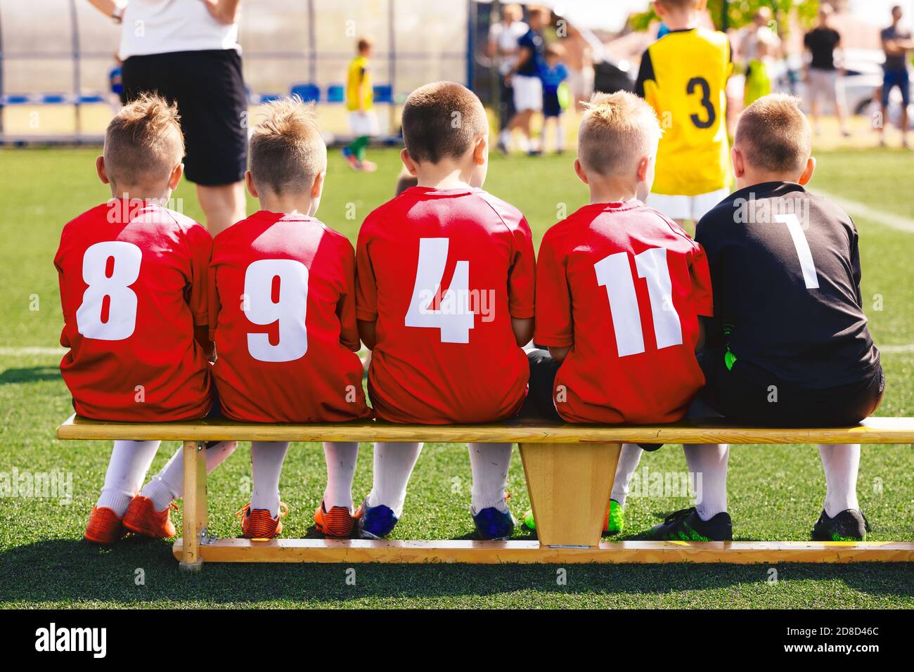 Équipe sportive de garçons en chemise rouge. Enfants assis sur un banc de football de substitution. Tournoi de football scolaire pour les enfants. Entraîneur de football et jeu de compétition en t Banque D'Images