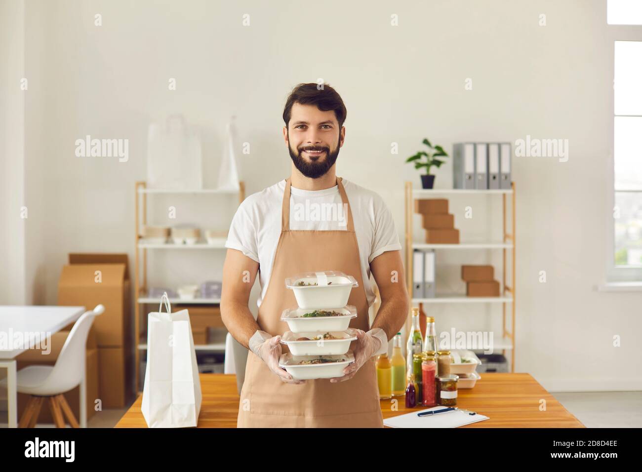 Employé souriant de café dans un uniforme de tablier tenant prêt déjeuner à emporter commandes dans des récipients alimentaires Banque D'Images