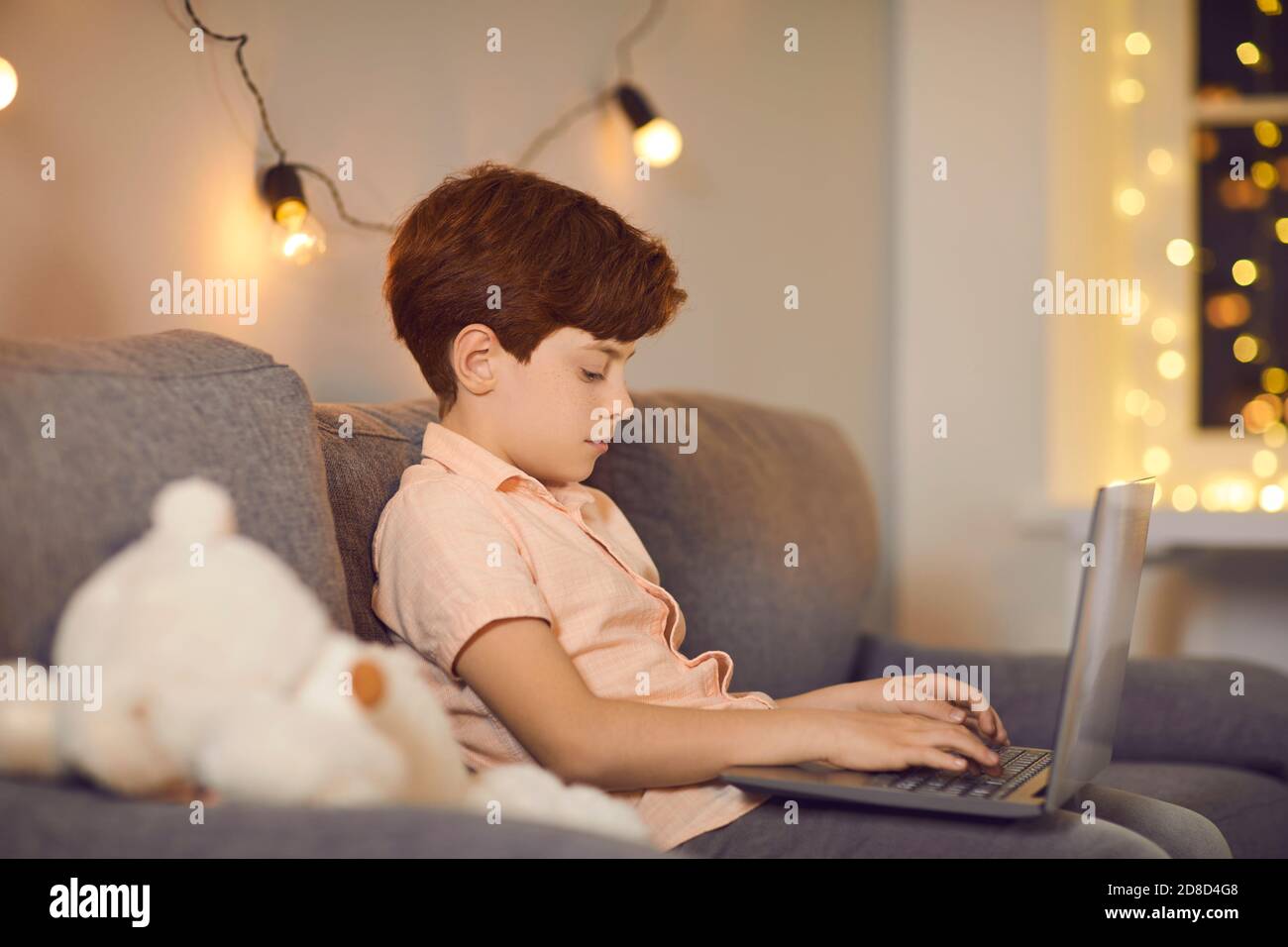 Garçon assis sur un canapé avec ordinateur portable et en train de taper le message pendant communication en ligne Banque D'Images