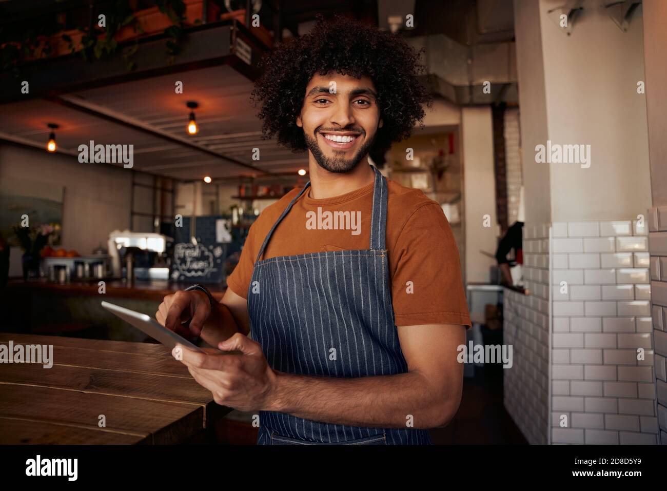 Portrait d'un beau jeune serveur masculin debout dans un café portant tablier tenant une tablette numérique Banque D'Images