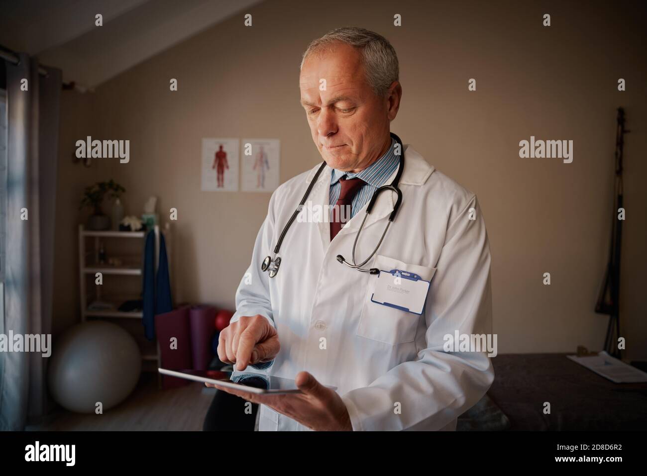 Professionnel de la santé masculin senior portant une blouse de laboratoire et un stéthoscope utilisant le numérique tablette Banque D'Images