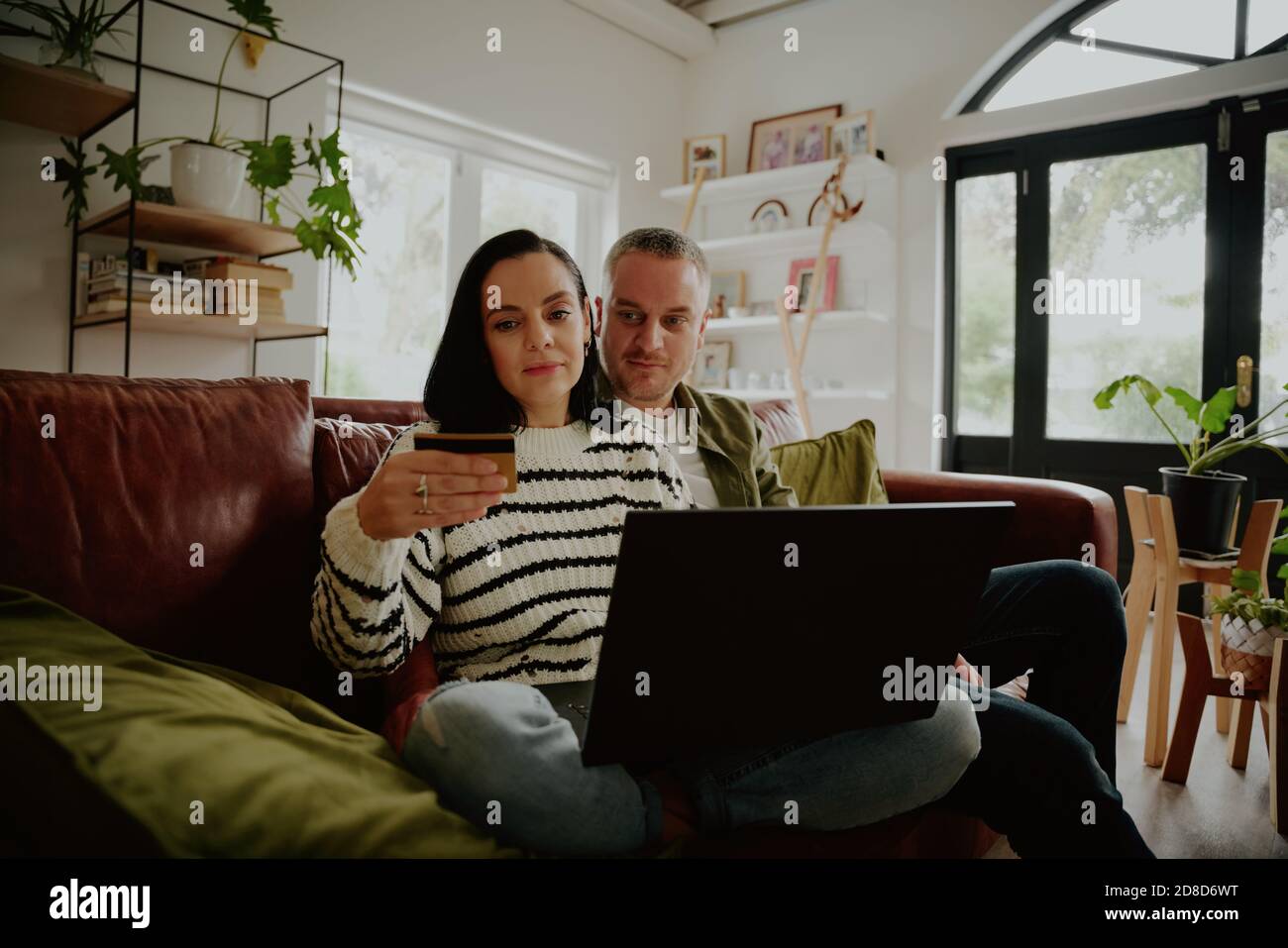 Jeune femme tenant une carte de débit pour effectuer une transaction d'achat en ligne avec mari à la maison Banque D'Images Jeune femme tenant une carte de débit pour effectuer une transaction d'achat en ligne avec mari à la maison Banque D'Images