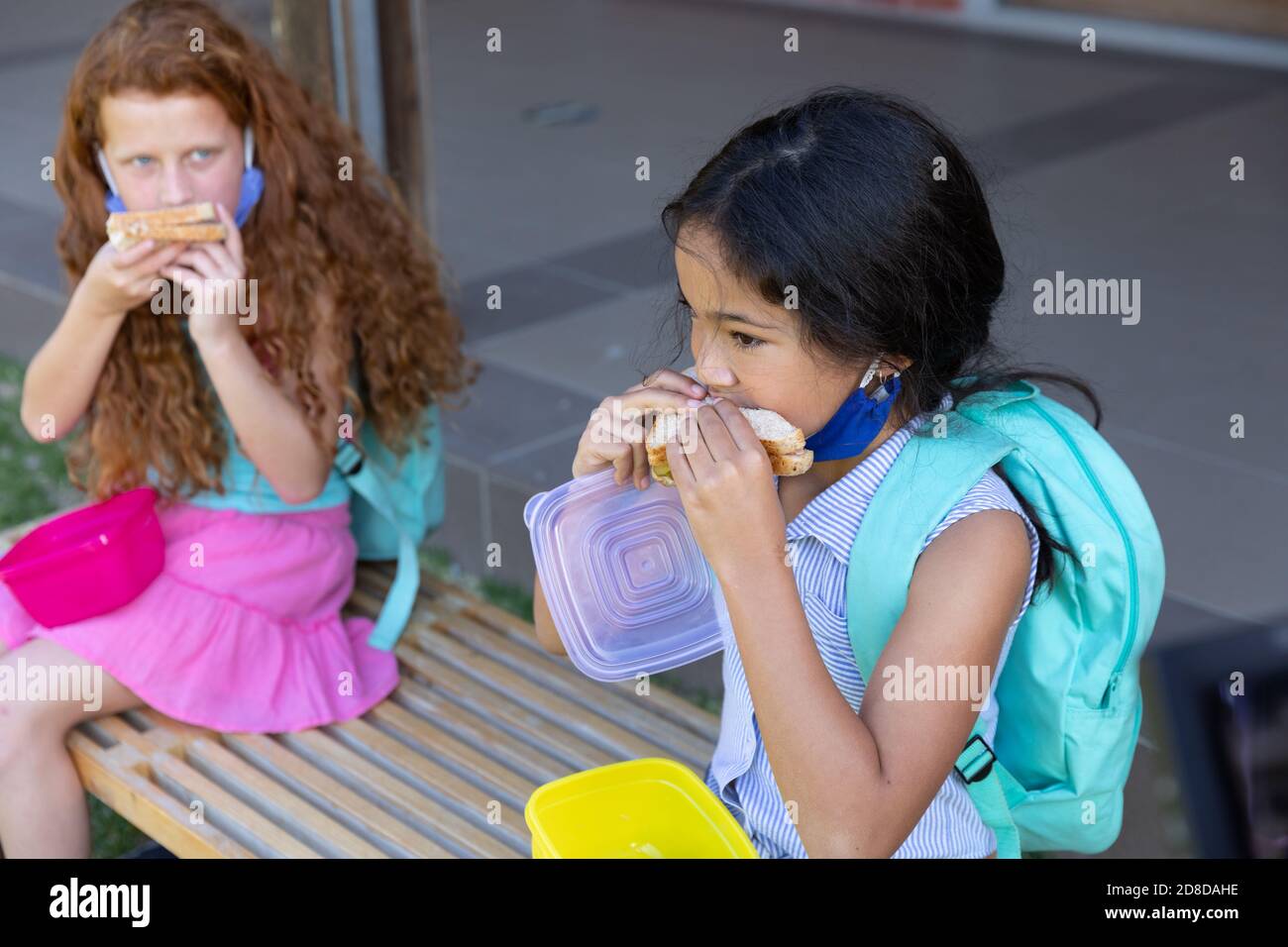 Deux filles mangent le déjeuner dans la boîte de tiffin tout en étant assise banc dans le parc à l'école Banque D'Images
