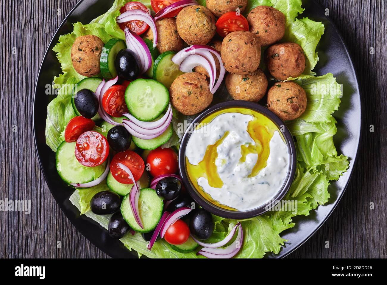 Assiette méditerranéenne de falafels, tomates, concombre, oignon rouge,  olives noires, sur les feuilles de salade fraîches servies avec de la sauce  tzatziki servie sur une sauce noire Photo Stock - Alamy