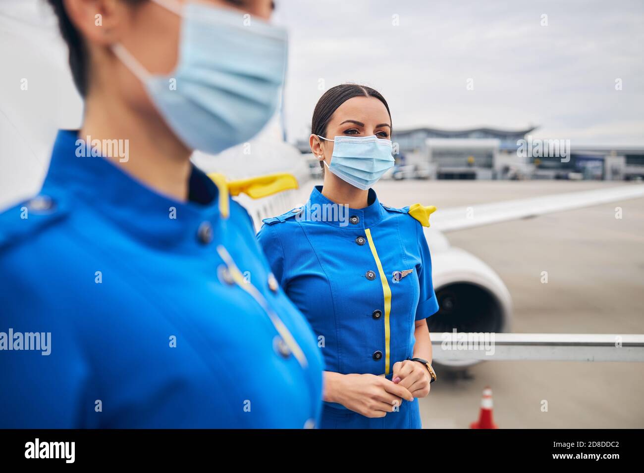Jeunes hôtesses rêveuses dans des revêtements de visage à l'aérodrome Banque D'Images