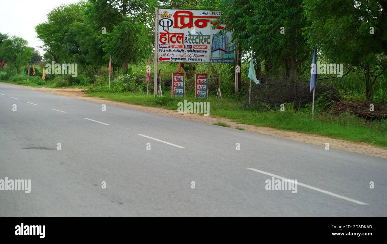 22 septembre 2020 : Mahroli, Rajasthan, Inde / route vide et panneau publicitaire. Vue sur la route rouge vide le matin avec ciel bleu au-dessus. Banque D'Images