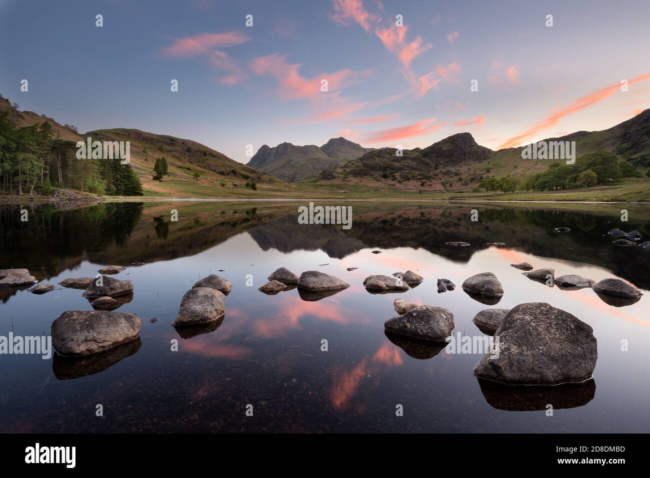 Reflet parfait d'un beau lever de soleil avec des rochers éparpillés en premier plan à Blea Tarn dans le Lake District, Royaume-Uni. Banque D'Images