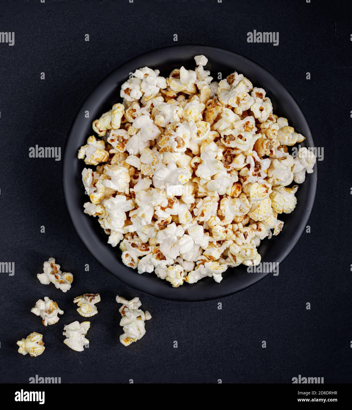 Parsemer de pop-corn salé dans un bol sur fond noir avec espace de copie. Vue sur le sommet du Popcorn fait maison. Banque D'Images