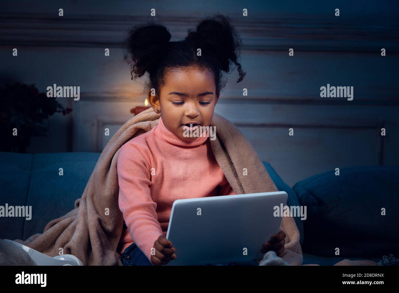 Bonne fillette afro-américaine lors d'un appel vidéo avec un ordinateur portable et des appareils domestiques, elle a l'air ravie et heureuse. Parlant à Santa avant la veille du nouvel an, sa famille, prenant la classe préscolaire en ligne. Banque D'Images