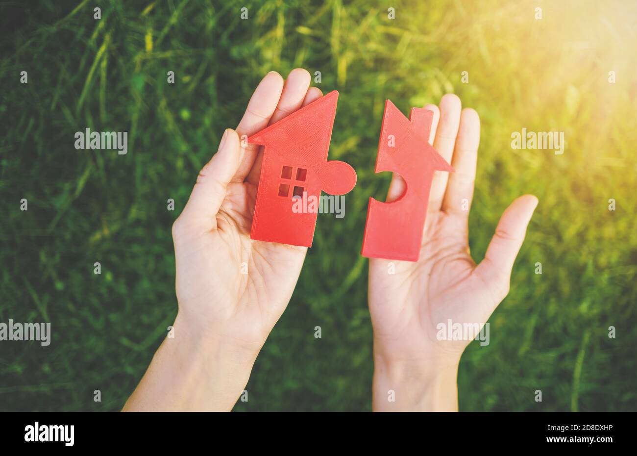 Maison rouge avec une forme de deux parties de puzzle dans les mains humaines. Banque D'Images