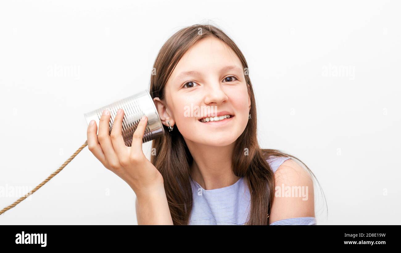 Une fille souriante avec une boîte peut téléphone près de l'oreille, jouant dans le chat rétro connecté. Enfant isolé sur fond blanc Banque D'Images