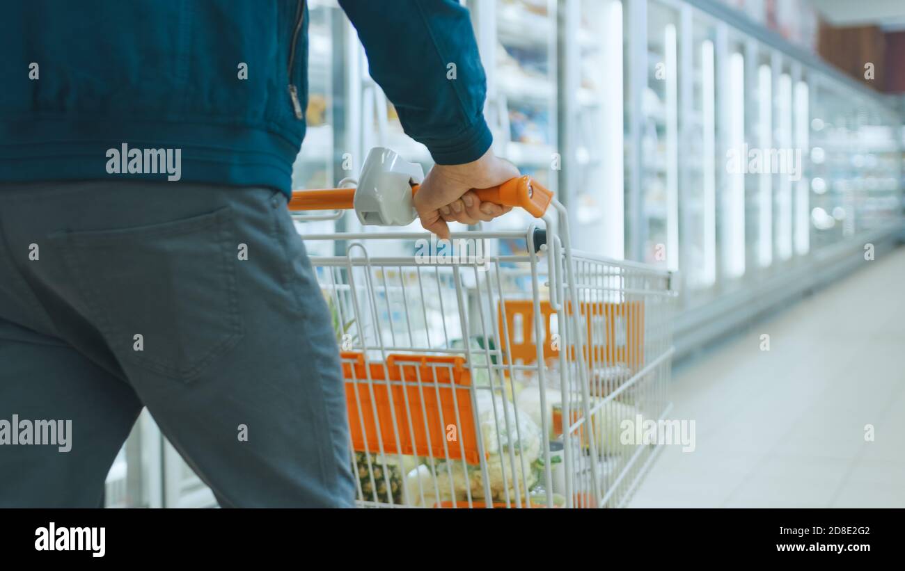 Tourné au supermarché : de l'homme poussant le chariot plein de produits par la section des produits surgelés et des produits laitiers du magasin. Banque D'Images