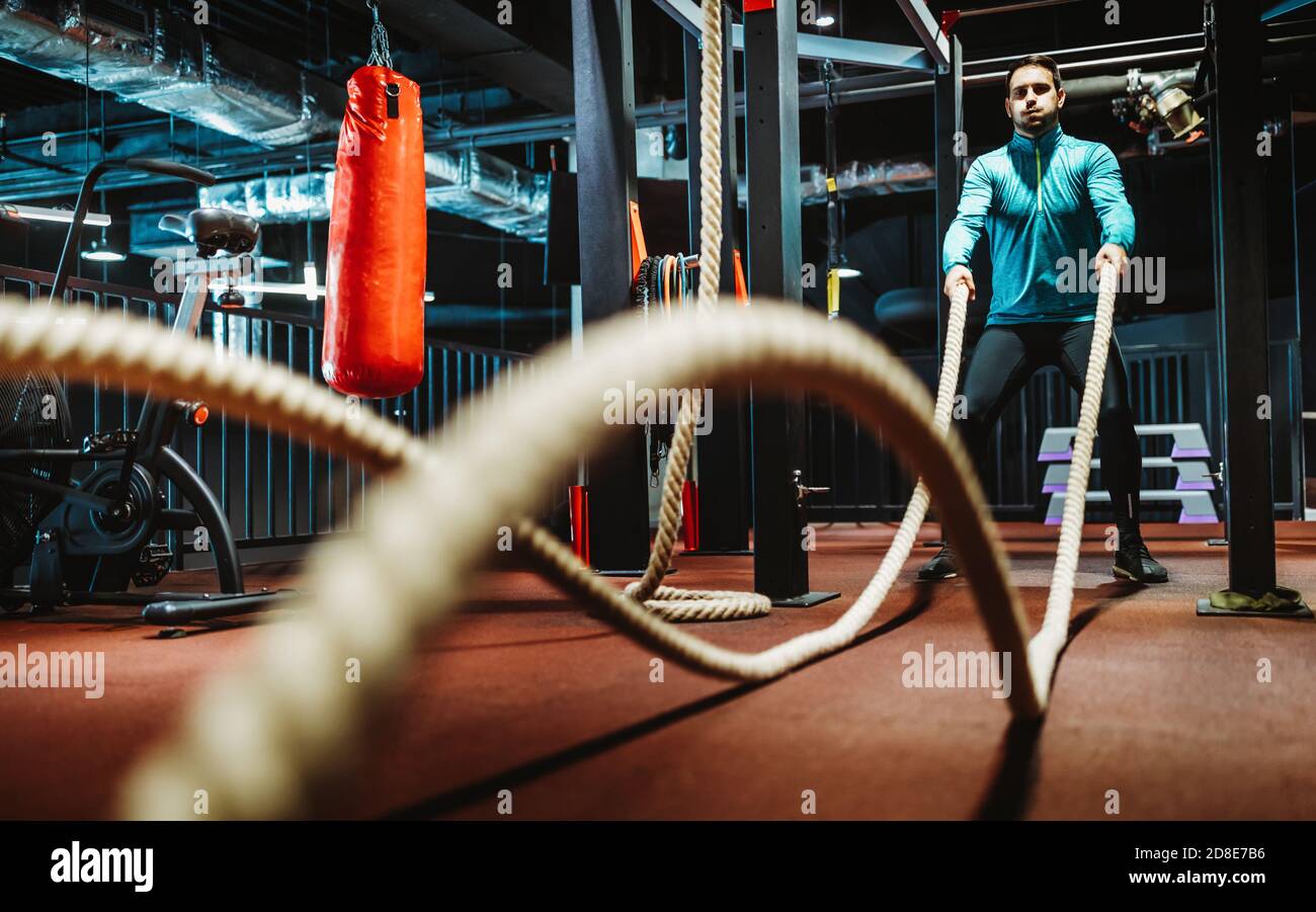 Homme de fitness s'entraîner avec des cordes de combat à la salle de gym. Banque D'Images