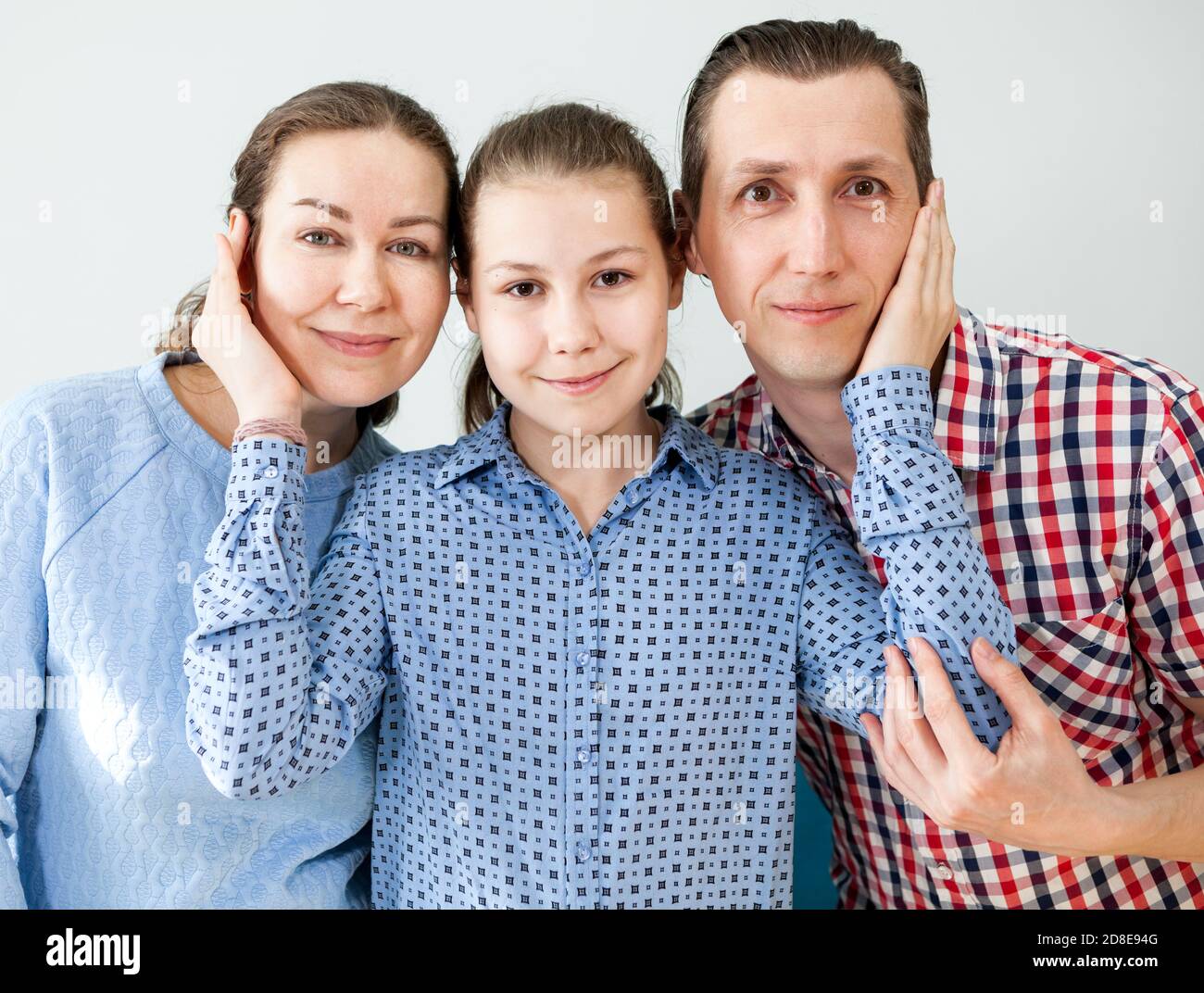 Père d'âge moyen, mère et fille pré-adolescent debout ensemble, fille tenant des parents sur la joue, regardant l'appareil photo Banque D'Images