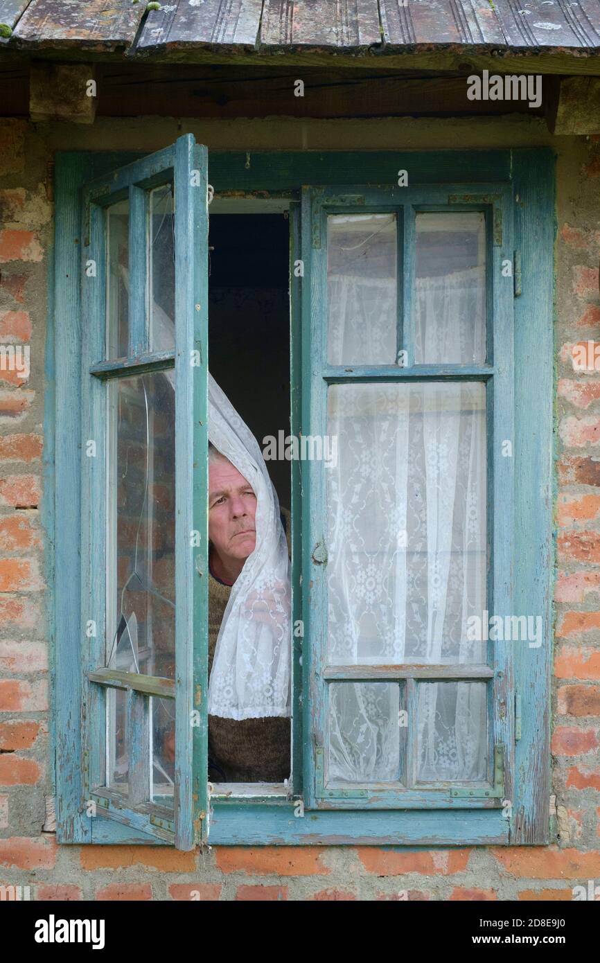 misérable à regarder les vieux twitcher de rideau mâle qui espionne les voisins de fenêtre pour trouver quiconque enfreint les règles de confinement en cas de pandémie du coronavirus Banque D'Images
