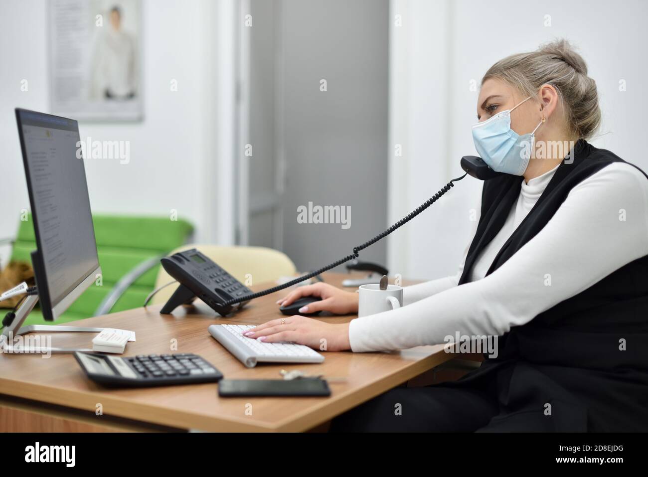 Une jeune femme responsable des ventes dans un masque de visage qui parle le téléphone au bureau Banque D'Images