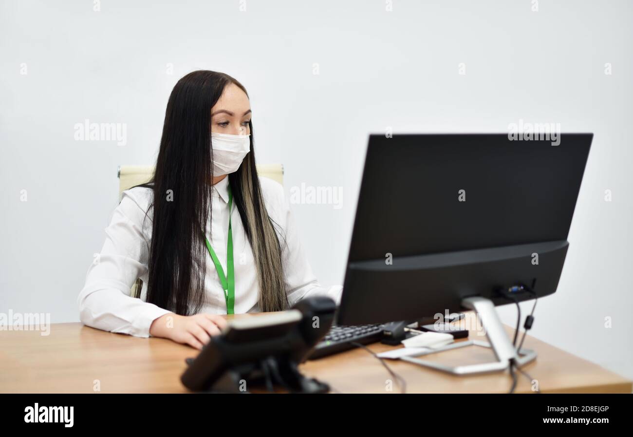 Une jeune femme employée de la banque dans un masque de visage travaille avec un ordinateur de bureau au bureau Banque D'Images